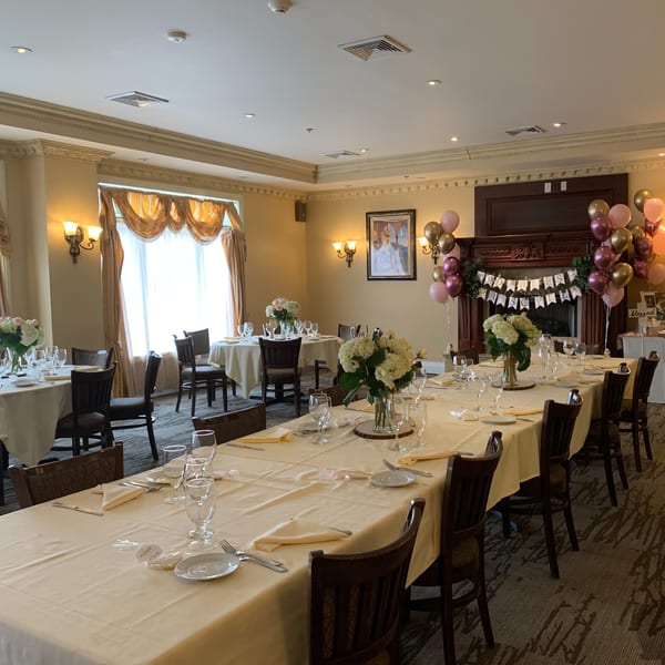 A Luciano's Ristorante dining room set for a party, with long tables, floral centerpieces, and balloons.