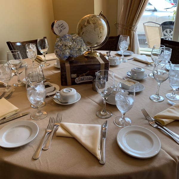 A round table set with plates, silverware, glasses, and a globe centerpiece with blue flowers.