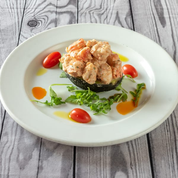 Shrimp salad in an avocado half, garnished with cherry tomatoes, arugula, and olive oil.