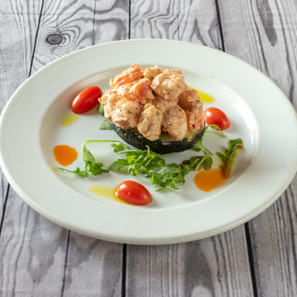 Shrimp salad in an avocado half, garnished with cherry tomatoes, arugula, and olive oil.