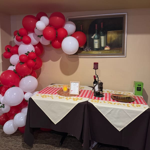 Red and white balloons frame a table with checkered cloths, a wine bottle, and a cocktail menu.