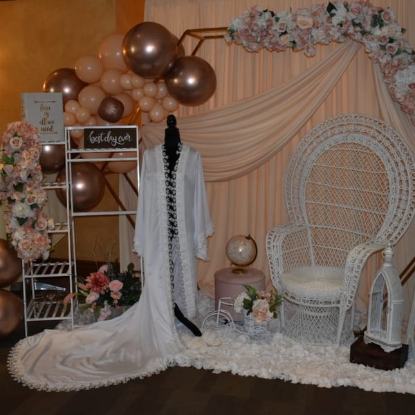 A bridal shower display with a white robe, wicker chair, balloons, and floral decorations.