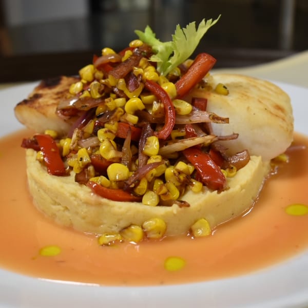 Grilled fish on a bed of polenta, topped with corn, red peppers, and onions, in a light sauce.