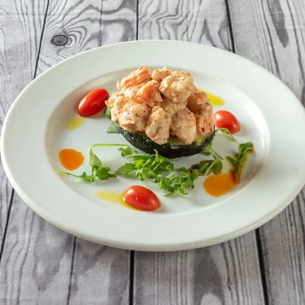Shrimp and avocado salad with cherry tomatoes and arugula on a white plate.