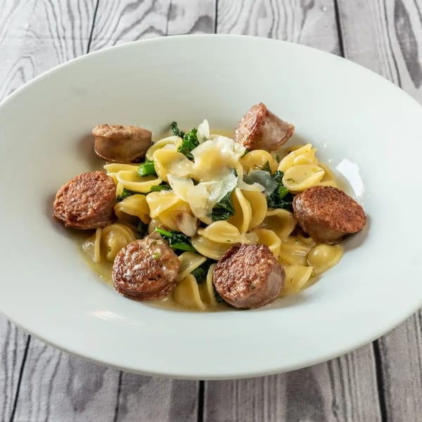 Orecchiette pasta with sausage, broccoli rabe, and shaved parmesan in a white bowl.