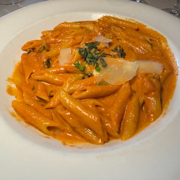 Penne pasta in a creamy orange sauce, garnished with fresh basil and shaved Parmesan cheese.