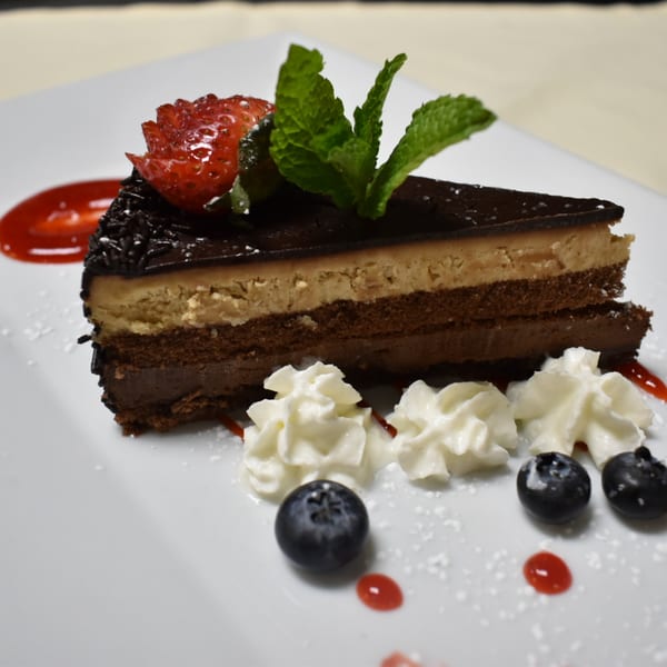 A slice of layered chocolate and peanut butter cake with strawberry, mint, whipped cream, and blueberries.