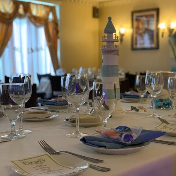 Set tables with wine glasses, blue napkins, and a lighthouse centerpiece at Luciano's Ristorante.