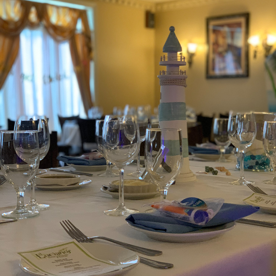 Set tables with wine glasses, blue napkins, and a lighthouse centerpiece at Luciano's Ristorante.