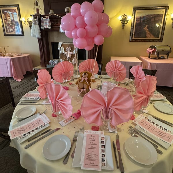 A baby shower table setting with pink decorations, a teddy bear centerpiece, and menus at Luciano's Ristorante.