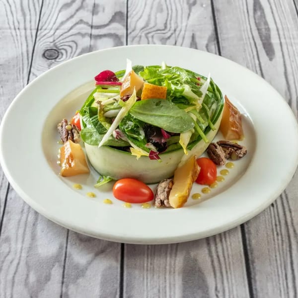 Luciano's Ristorante & Lounge's fresh green salad with tomatoes, pecans, and cheese on a white plate.