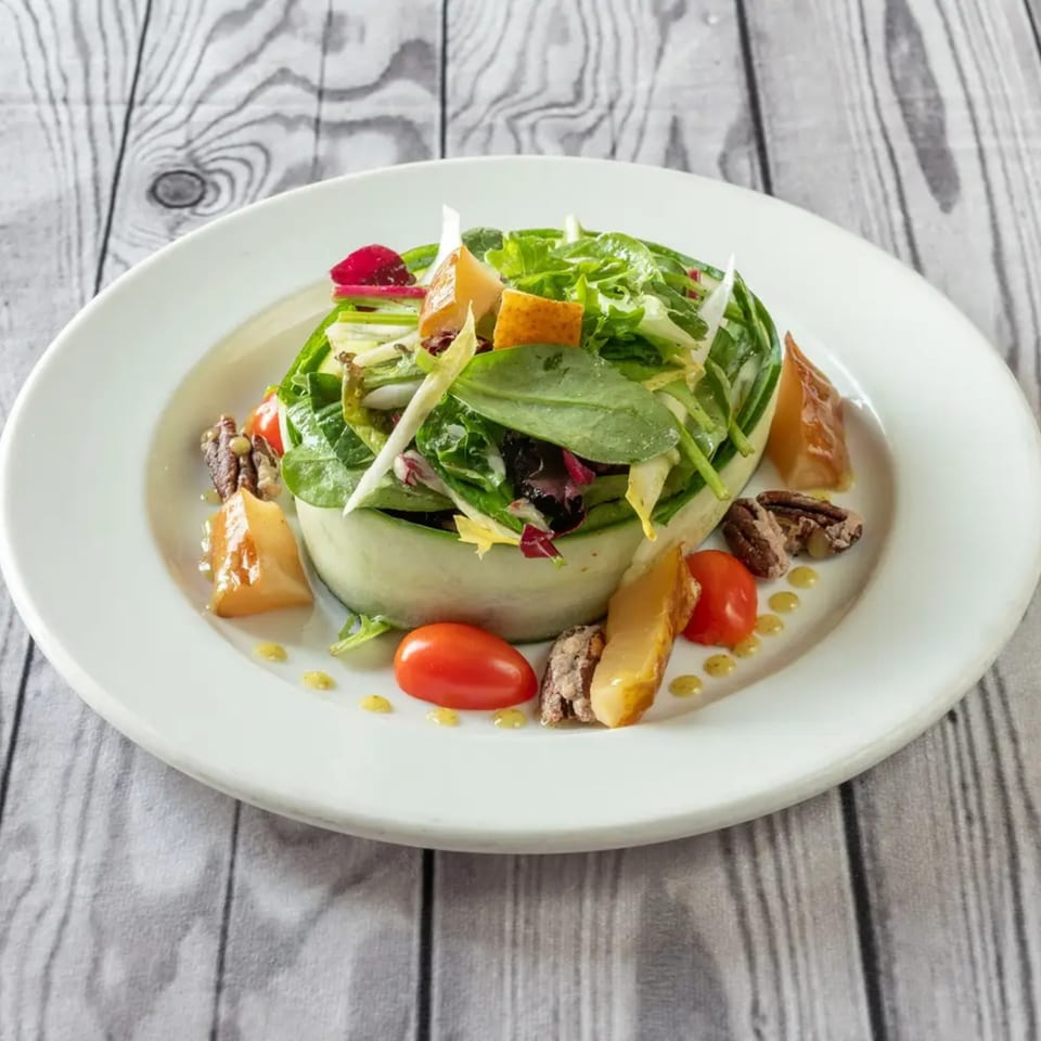 Luciano's Ristorante & Lounge's fresh green salad with tomatoes, pecans, and cheese on a white plate.