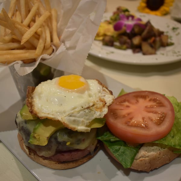 Gourmet burger with fried egg, avocado, and tomato, served with a side of golden french fries.