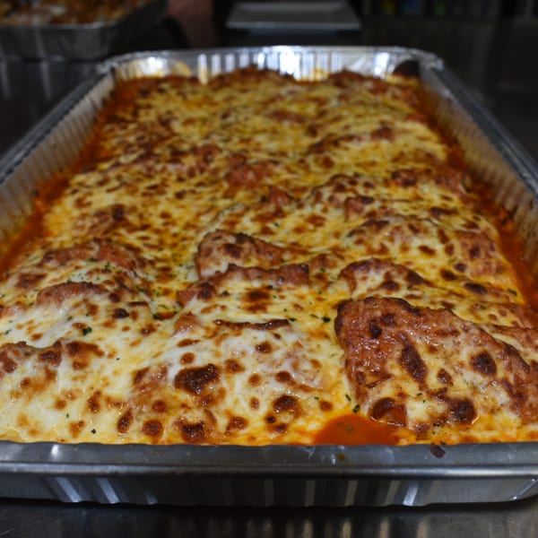 Large pan of Luciano's baked lasagna with melted, bubbly cheese and rich tomato sauce.