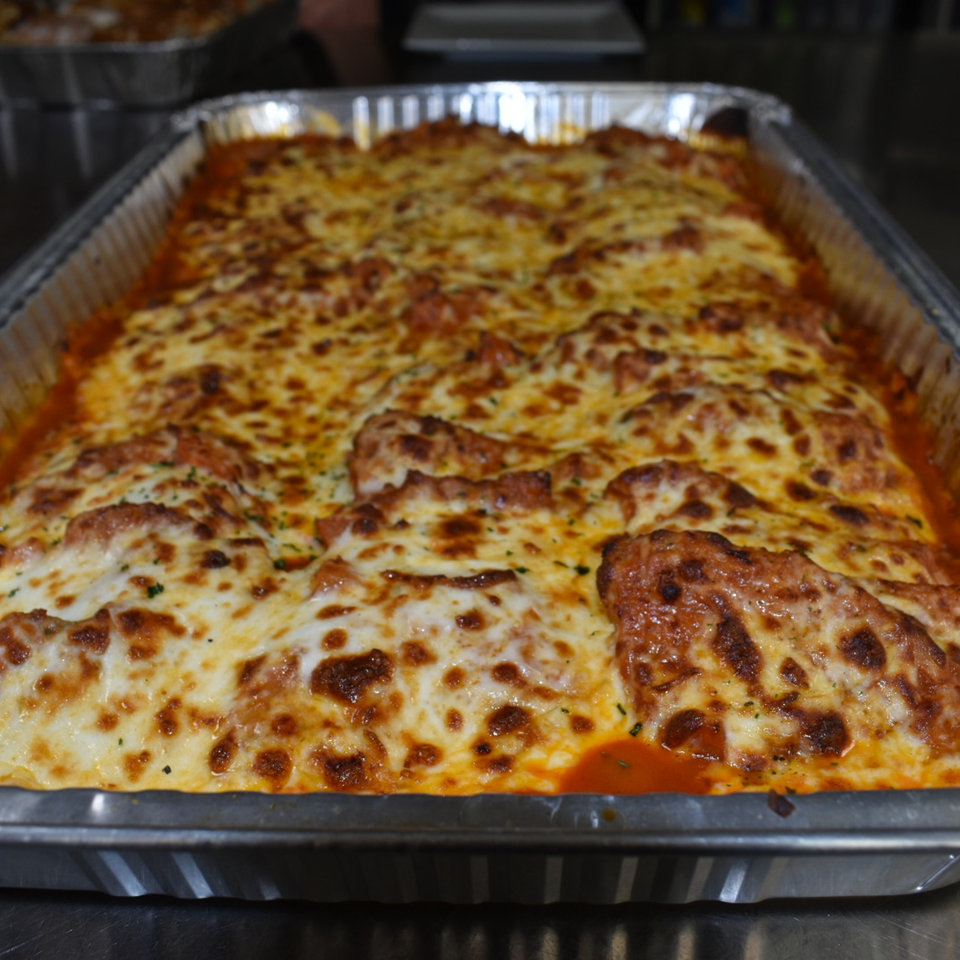 Large pan of Luciano's baked lasagna with melted, bubbly cheese and rich tomato sauce.