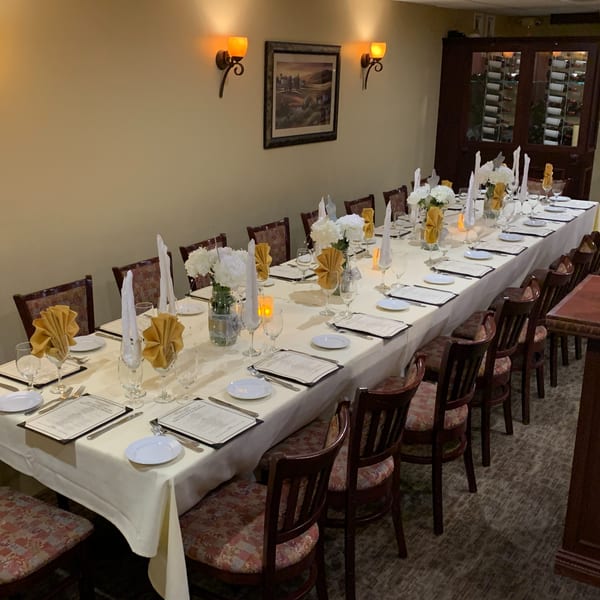 A long dining table set for a banquet with white tablecloths, gold napkins, and floral centerpieces.