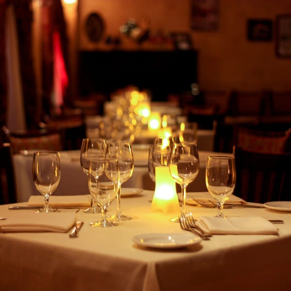 A dimly lit Luciano's Ristorante dining table set with wine glasses, white napkins, and a glowing candle.
