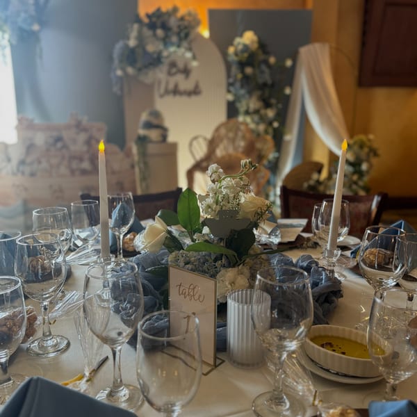 Elegant table setting with white and blue floral centerpiece, candles, wine glasses, and a table number.