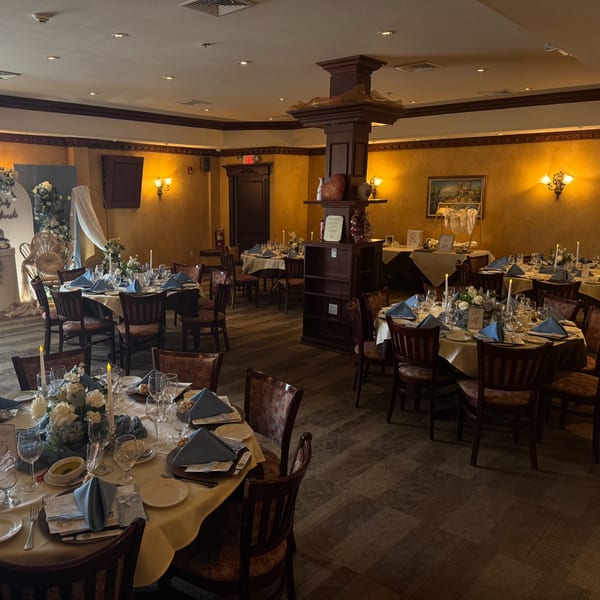 A restaurant dining room set for an event with round tables, blue napkins, and floral centerpieces.