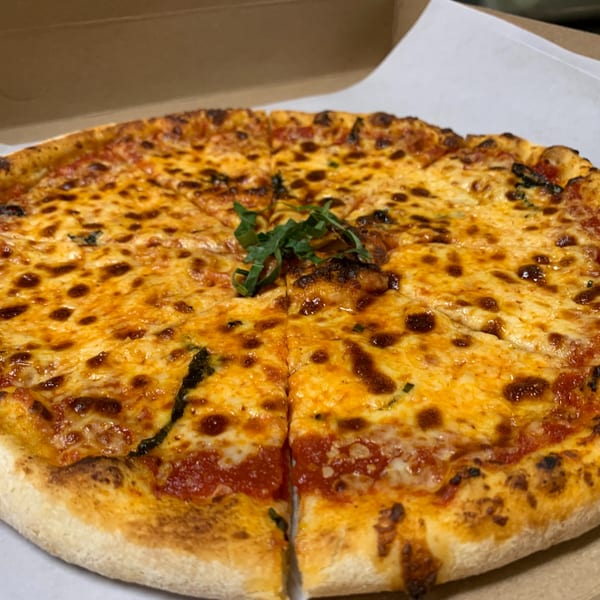 A whole, sliced Luciano's Ristorante & Lounge Margherita pizza with basil in a takeout box.