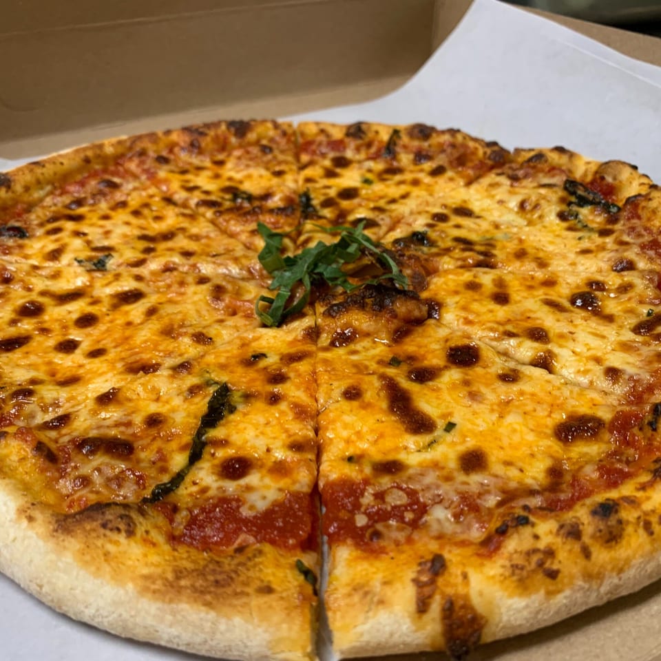A whole, sliced Luciano's Ristorante & Lounge Margherita pizza with basil in a takeout box.