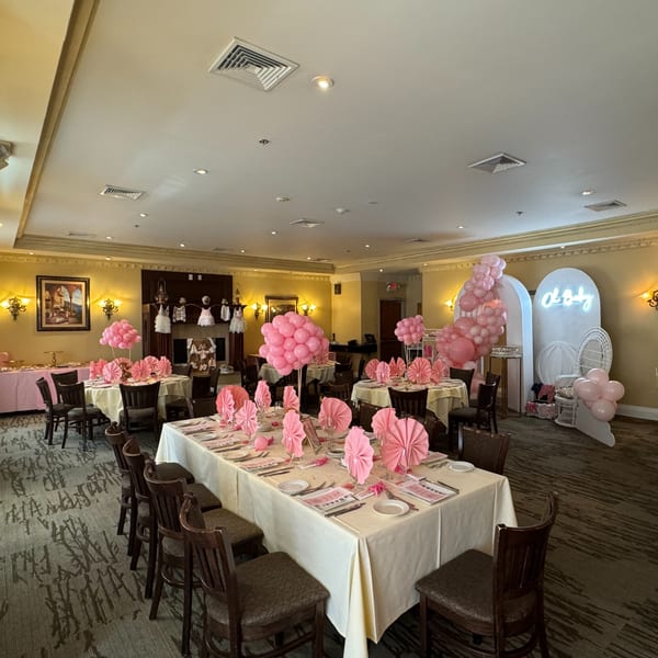 A Luciano's Ristorante dining room set for a baby shower with pink balloons and decor.