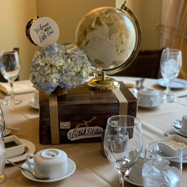 Table setting with a globe, blue hydrangeas, and a "Welcome to the World Little One" sign.