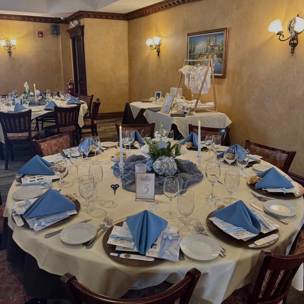 A restaurant dining room set for a baby shower with round tables, blue napkins, and floral centerpieces.