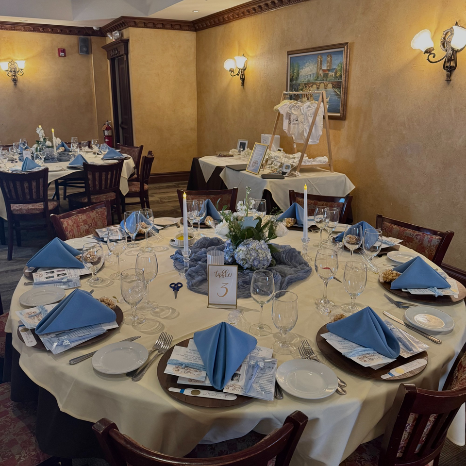 A restaurant dining room set for a baby shower with round tables, blue napkins, and floral centerpieces.