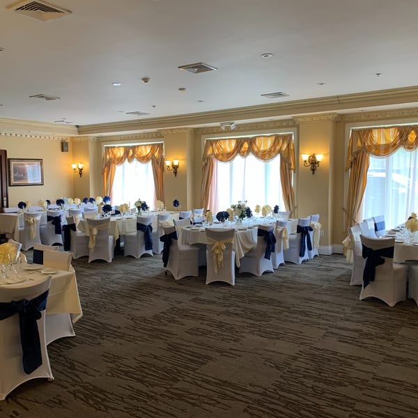 Elegant dining room at Luciano's Ristorante with round tables, white chairs, and blue and gold accents.