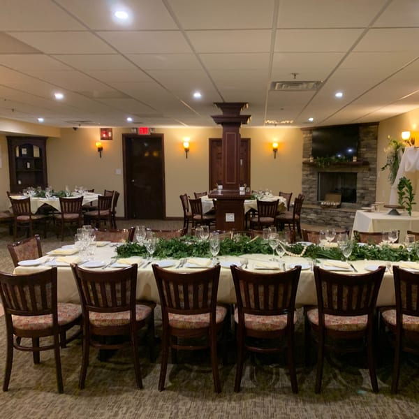 A formal dining room at Luciano's Ristorante with long tables set with white tablecloths and greenery.