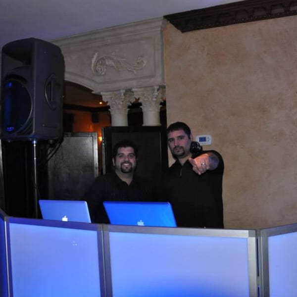 Two DJs with laptops and speakers at Luciano's Ristorante & Lounge, one pointing at the viewer.