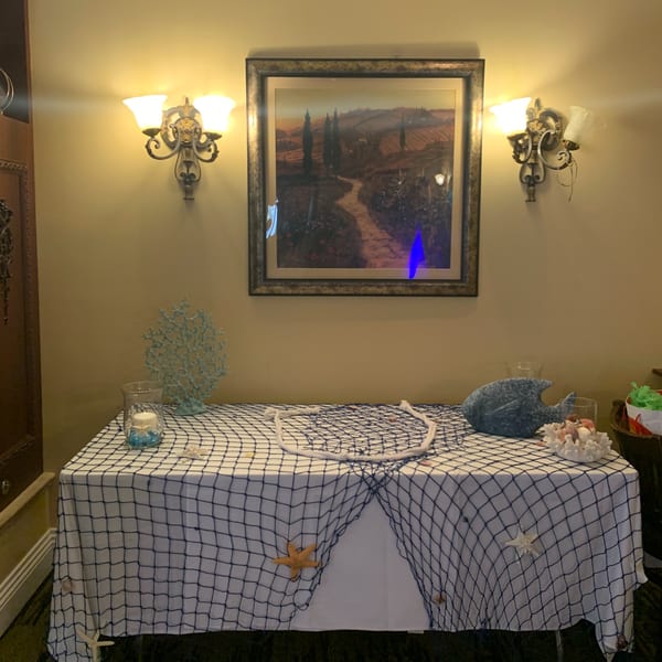 A table with a fishing net tablecloth, nautical decorations, and an Italian landscape painting above.