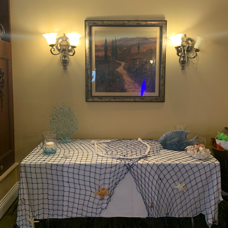 A table with a fishing net tablecloth, nautical decorations, and an Italian landscape painting above.