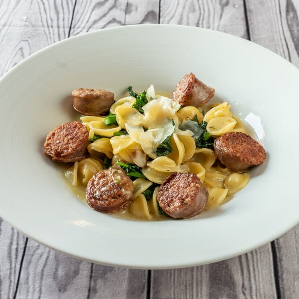 Orecchiette pasta with sausage, broccoli rabe, and shaved parmesan in a white bowl.