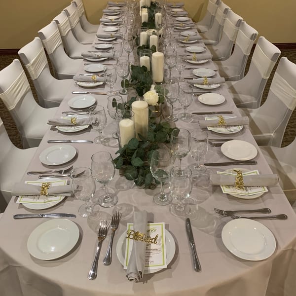 Long dining table set with white plates, silverware, wine glasses, and a green garland with candles.
