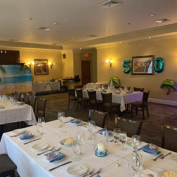 A Luciano's Ristorante dining room set for a party with white tablecloths, blue napkins, and beach-themed decor.