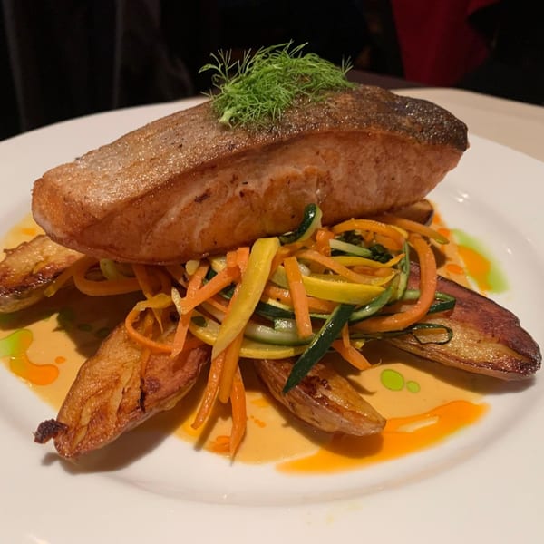 Pan-seared salmon with julienned vegetables, roasted potatoes, and sauce on a white plate.