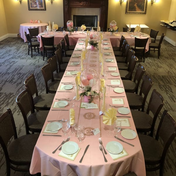 Long dining tables set with pink tablecloths, place settings, and balloon centerpieces in a restaurant.