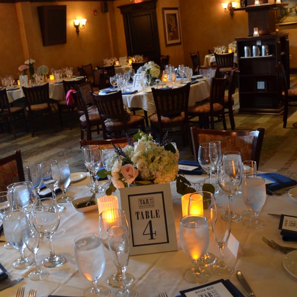 Elegantly set dining tables with white tablecloths, floral centerpieces, and glowing candles at Luciano's Ristorante.