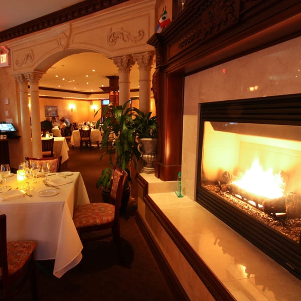 Cozy Luciano's Ristorante dining room with a lit fireplace, set tables, and warm lighting.
