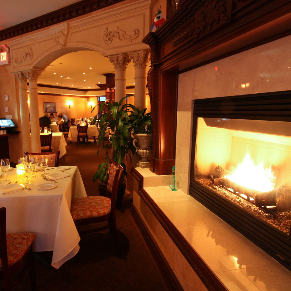Cozy Luciano's Ristorante dining room with a lit fireplace, set tables, and warm lighting.