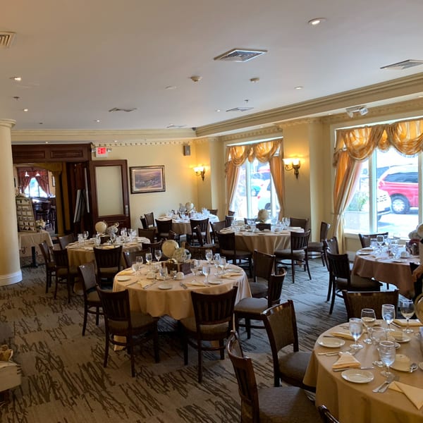Elegant dining room at Luciano's Ristorante with round tables set with white tablecloths and dark chairs.