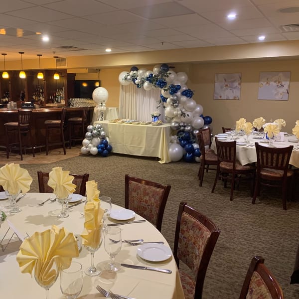 Luciano's Ristorante & Lounge dining room set for an event with tables, chairs, and a balloon arch.