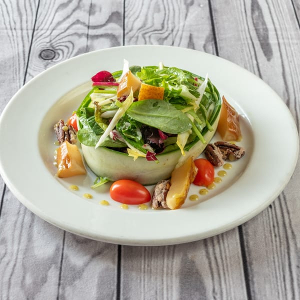 Luciano's Ristorante & Lounge's fresh green salad with cucumber, tomatoes, pecans, and cheese on a white plate.