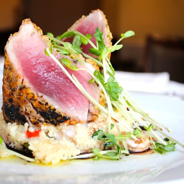 Seared tuna steak with a crispy crust, served over couscous and shrimp, garnished with microgreens.