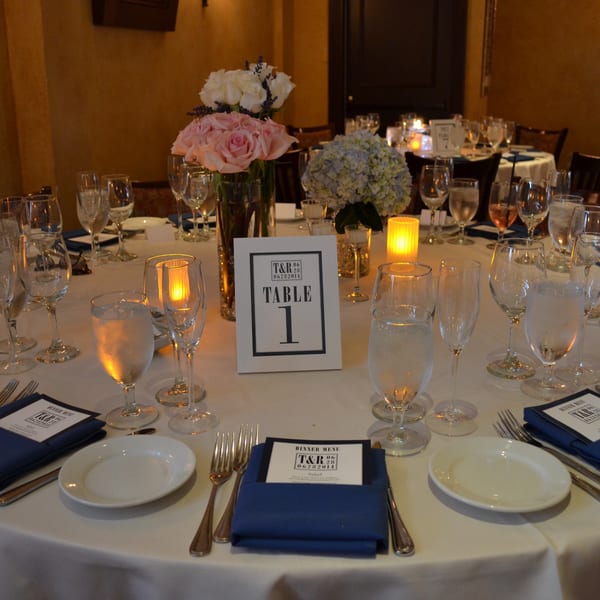 Elegantly set dining table with white tablecloths, blue napkins, flowers, and glowing candles at Luciano's Ristorante.