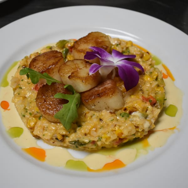 Seared scallops on a bed of creamy risotto with corn, garnished with arugula and an orchid.