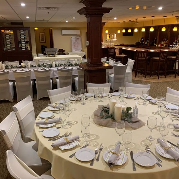 A banquet room with round tables set for dining, a buffet table, and a bar area.