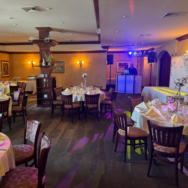 An Italian restaurant dining room set for an event, with tables, chairs, and a DJ booth with blue lights.